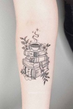 a black and white tattoo on the leg of a woman with books, coffee cup and flowers