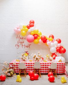 the table is set up for a party with red and yellow balloons, white checkered tablecloths, and flowers