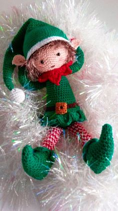 a crocheted elf doll laying on top of white tinsel with green and red plaid pants