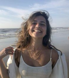 a woman standing on top of a sandy beach next to the ocean with her hair blowing in the wind