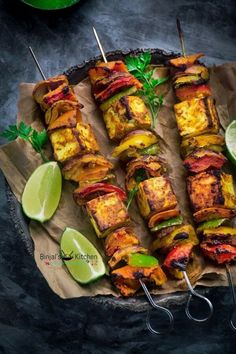 several skewers with meat and vegetables on them next to some lime wedges