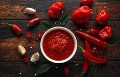 red peppers and garlic on a wooden table with sauce in a white bowl next to them