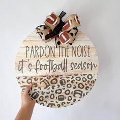 a hand holding a wooden sign that says pardon the noise it's football season