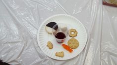 a paper plate topped with cookies and crackers next to a cup of wine on a plastic table cloth