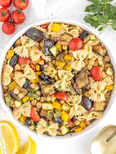 a white bowl filled with pasta salad next to sliced lemons, tomatoes and parsley