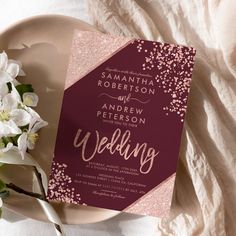 a wedding card on a plate next to some flowers and a white cloth with pink glitters