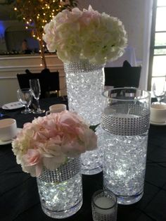 three tall vases filled with flowers on top of a black tablecloth covered table