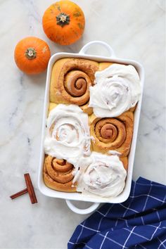 cinnamon rolls in a baking dish with icing and two pumpkins on the side