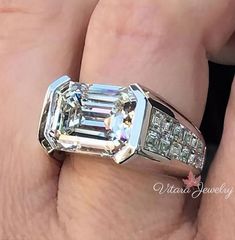 a person's hand holding a ring with an emerald and diamond set in it