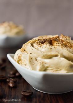 two white bowls filled with food on top of a wooden table next to coffee beans