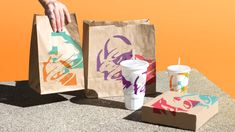 two paper bags with designs on them, one is holding a drink and the other has a cup