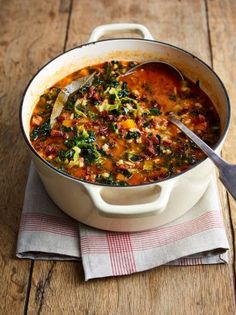 a large pot filled with soup on top of a wooden table next to a spoon