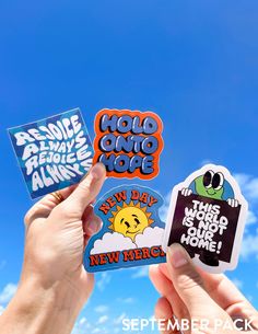 someone holding up some stickers in front of a blue sky with clouds and sun