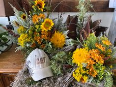 a baseball cap sits on top of some dried flowers and grass in front of a wooden table