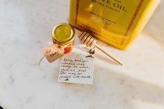 a honey jar with a note attached to it sitting on a counter next to a bottle of olive oil