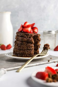 a stack of chocolate pancakes topped with strawberries on a white plate next to a fork