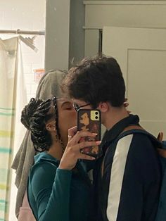 a young man and woman kissing in front of a mirror while taking a selfie