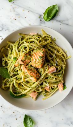 pasta with salmon and pesto in a white bowl on a marble table top next to basil leaves