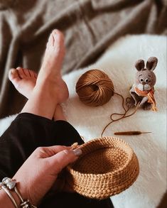 a woman is knitting with her feet up on the bed next to some yarn and a mouse