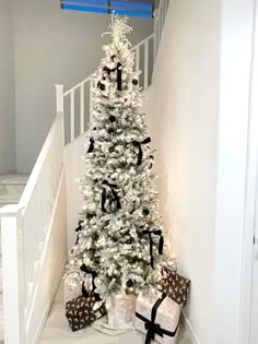 a white christmas tree with black bows and presents under the bannister railings