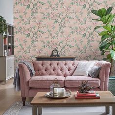 a living room with pink couches and wallpaper on the walls in front of a coffee table