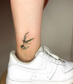 a small tattoo on the ankle of a woman's foot with an olive branch