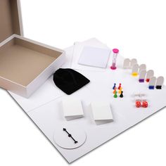 an open box with several different items on the table next to it, including pens and magnets