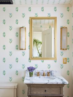 a bathroom with a mirror, sink and wallpaper in the background that has green leaves on it