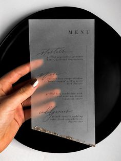 a person holding up a piece of paper on top of a black plate with writing on it