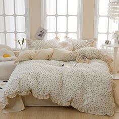 a bed with white and beige comforters in front of two large windows on the floor