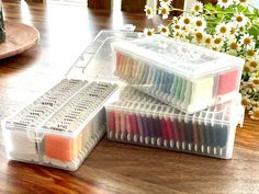 two plastic storage containers filled with different colored threads on a wooden table next to flowers