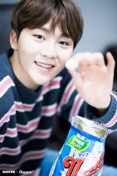 a young man in striped shirt holding up an unopened can of drink and pointing to the camera