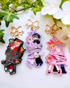 three key chains with anime characters on them next to some white flowers and green leaves