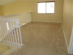 an empty living room with stairs leading up to the second floor, and a window on the far wall