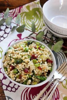 a white bowl filled with rice and vegetables next to a fork on top of a table