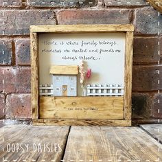 a wooden frame with a small house and fence on it that says, here is where family belongs