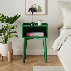 a green nightstand with books on it next to a bed and potted plant in the corner