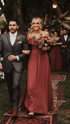 a man and woman in formal wear walking down the aisle at an outdoor wedding ceremony