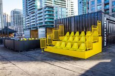 several yellow chairs sitting on top of a cement floor next to tall buildings in the background