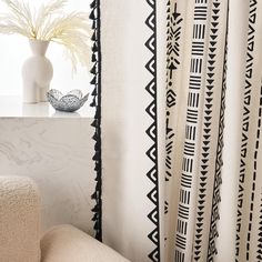 a white vase sitting on top of a table next to a black and white curtain