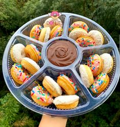 a person holding a tray with donuts and dipping sauce on it in front of some trees