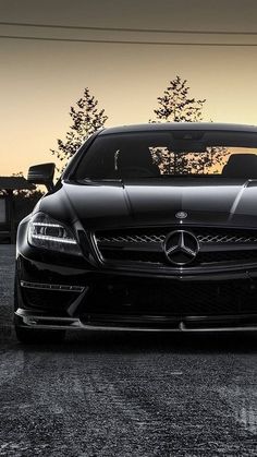 the front end of a black sports car parked in a parking lot at sunset or dawn