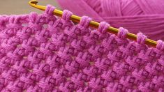 the crochet stitch is being worked on with a knitting needle and yarn ball in the background