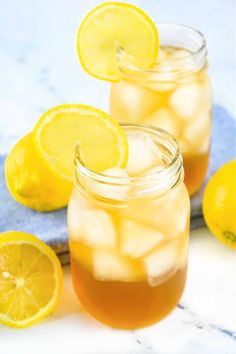 two mason jars filled with lemonade and ice next to sliced lemons on a blue towel