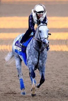 a man riding on the back of a white horse across a dirt field at sunset