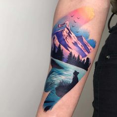 a woman's arm with a mountain and lake tattoo on the left upper arm