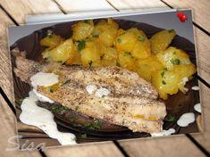 fish and potatoes are on a plate with white sauce in the middle, sitting on a wooden table