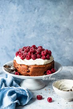 a cake with white frosting and raspberries on top is sitting on a plate