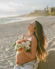 a pregnant woman sitting on the beach with flowers