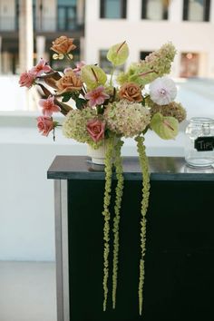 a vase filled with lots of flowers on top of a black counter next to a building